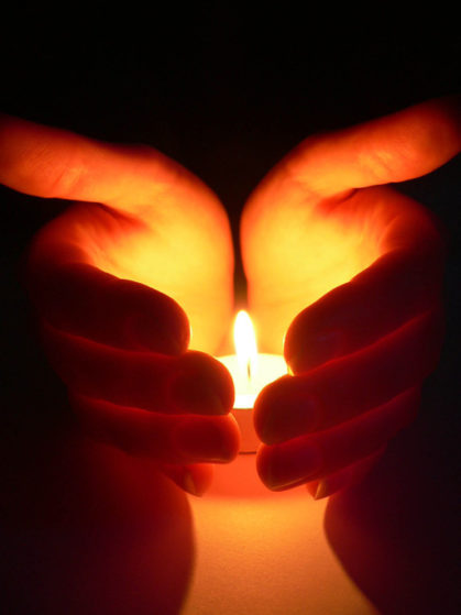 A photo of a persons hands cradling a lit candle.