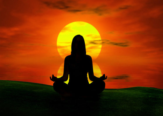 A silhouette of a female meditating and framed by the setting sun.