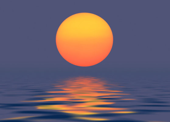 A photo of a golden setting sun reflecting in the calm ocean.
